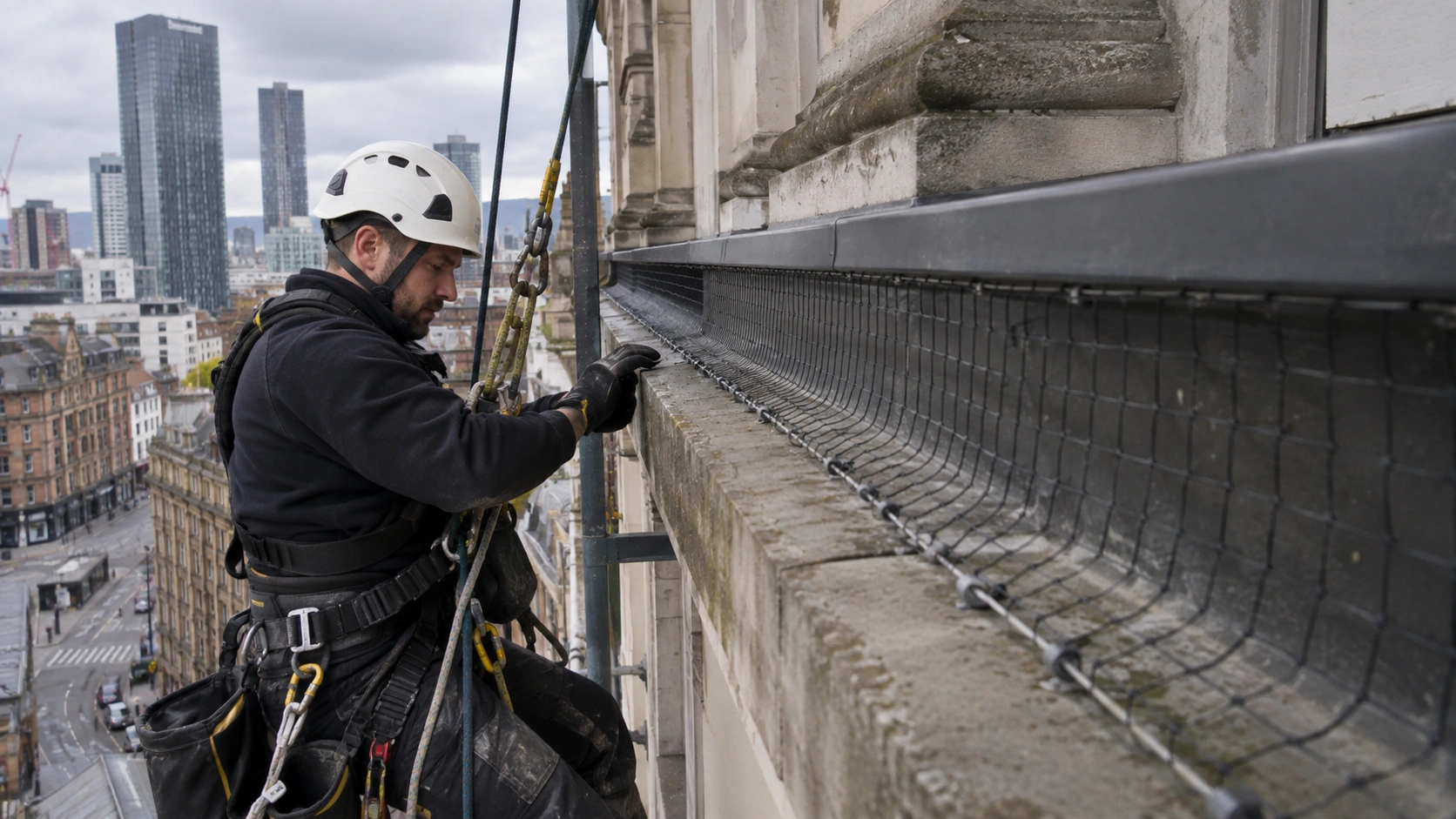 bird netting installed on a commercial building ledge or parapet, with a rope-access technician working nearby
