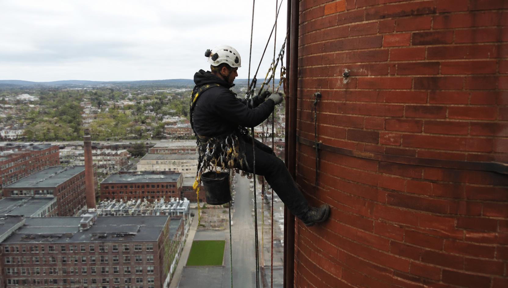 Steeplejack using rope access to work at height on a tall brick industrial chimney