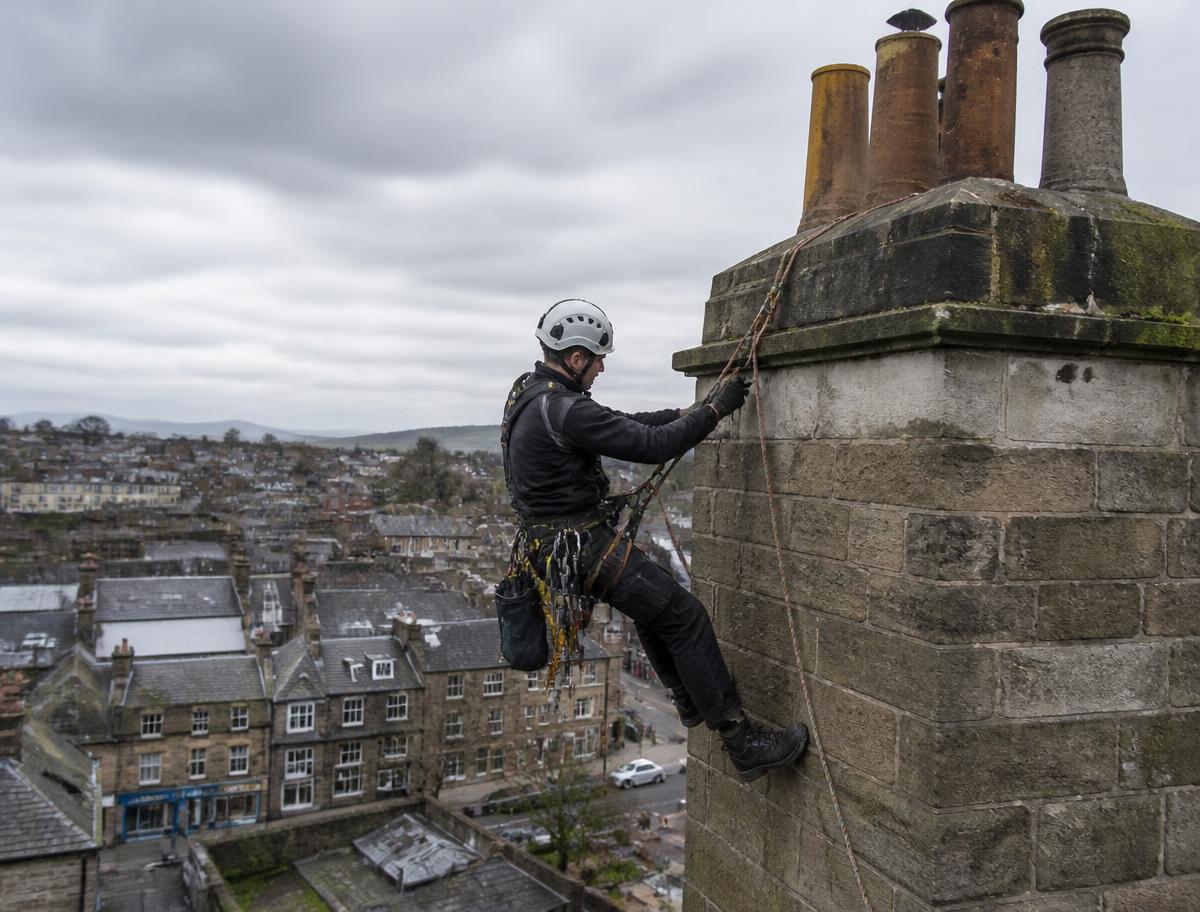 Rope access technician inspecting a chimney stack on an older stone commercial building