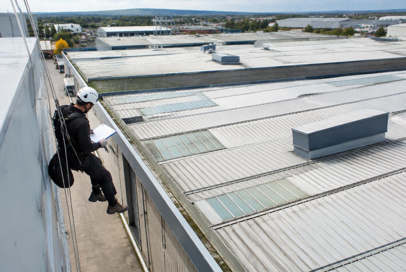 Rope-access technician surveying multiple elements of an industrial roof
