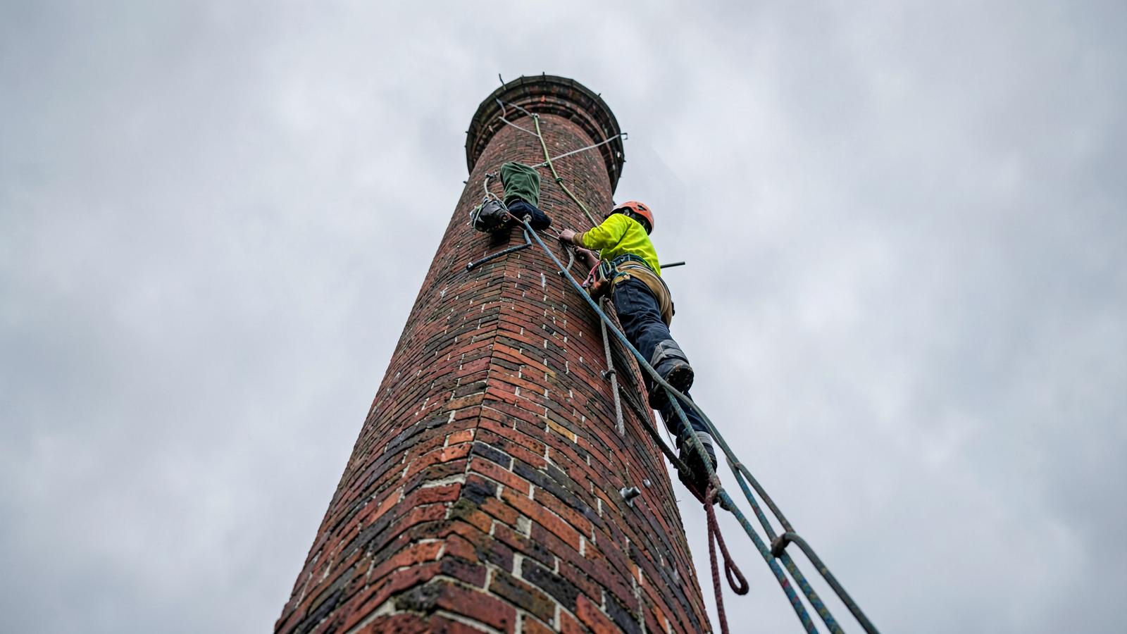 Rope-access steeplejack working at height on a tall industrial chimney