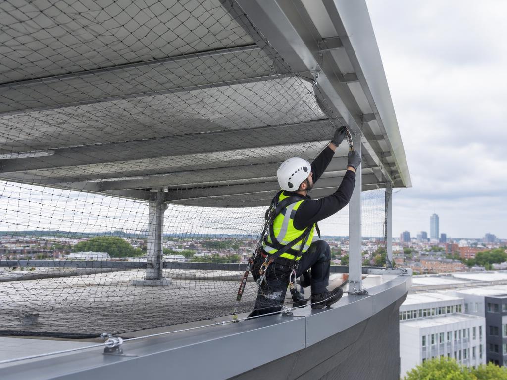Working-at-height technician installing bird netting around a commercial roof