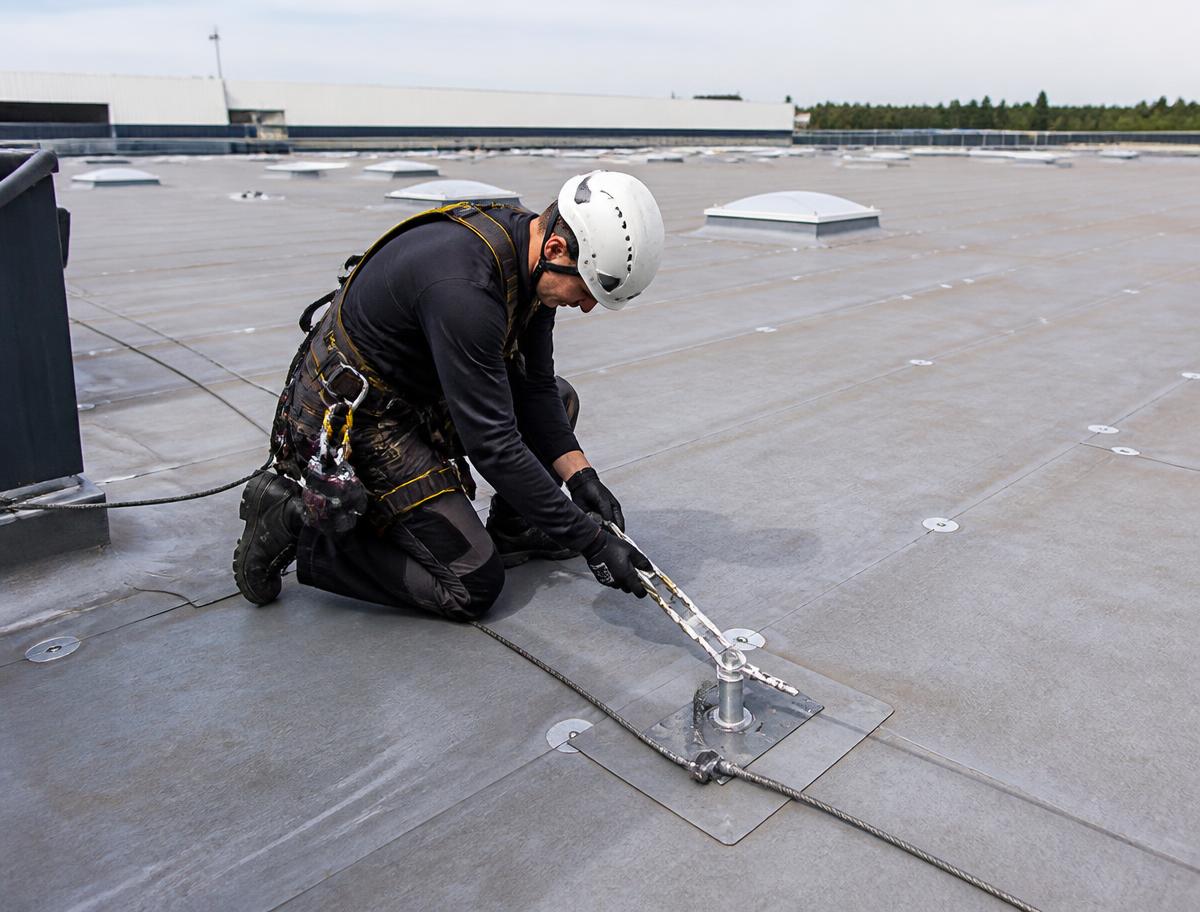 Technician using rope access equipment on a large flat industrial warehouse roof